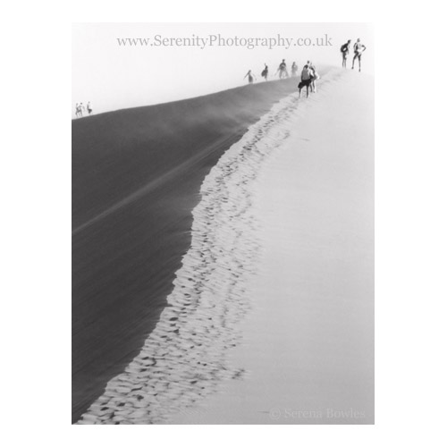 Small figures climb up the sand of Dune 45, Sousselvei, Namibia, as the wind blows.